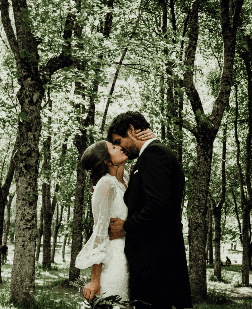 foto de una pareja vestida de novios dandose un beso en el bosque